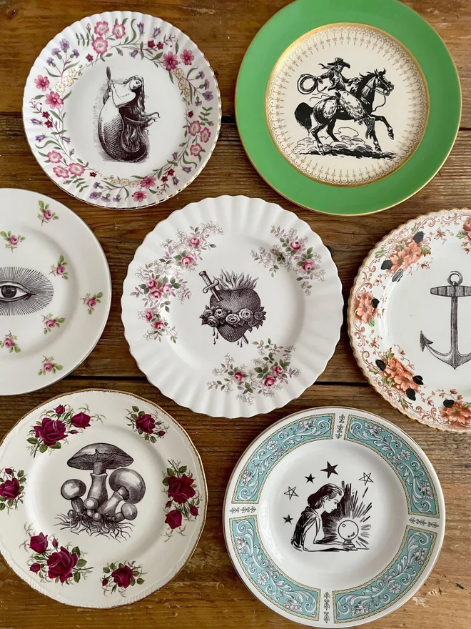 an eclectic collection of vintage plates hung together on a white wall, each plate is different with patterned or gold borders and vintage images in their centres