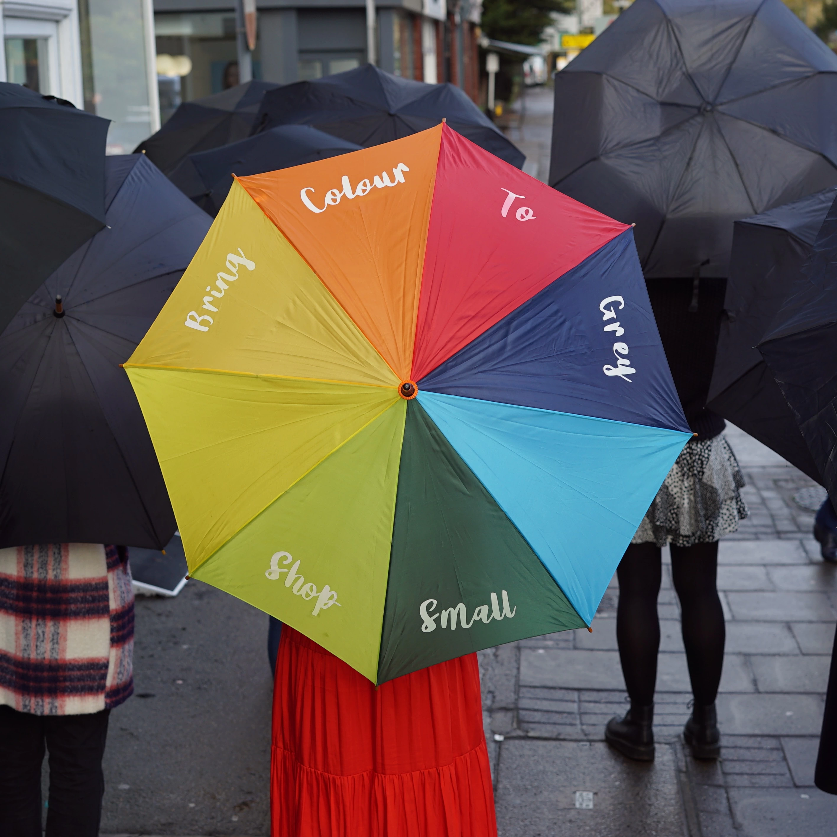 A colourful umbrella amongst many black umbrellas that says 'Bring Colour to Grey'