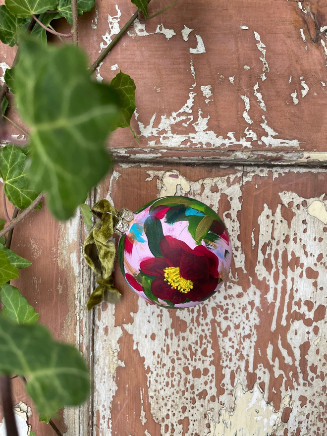 hand painted christmas bauble pale pink background adorned with deep red camellia flowers