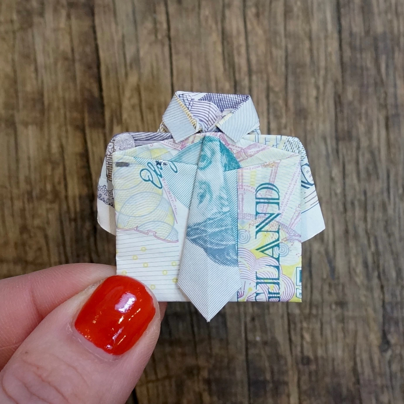 Woman's hand holing an origami shirt made from a five pound note 