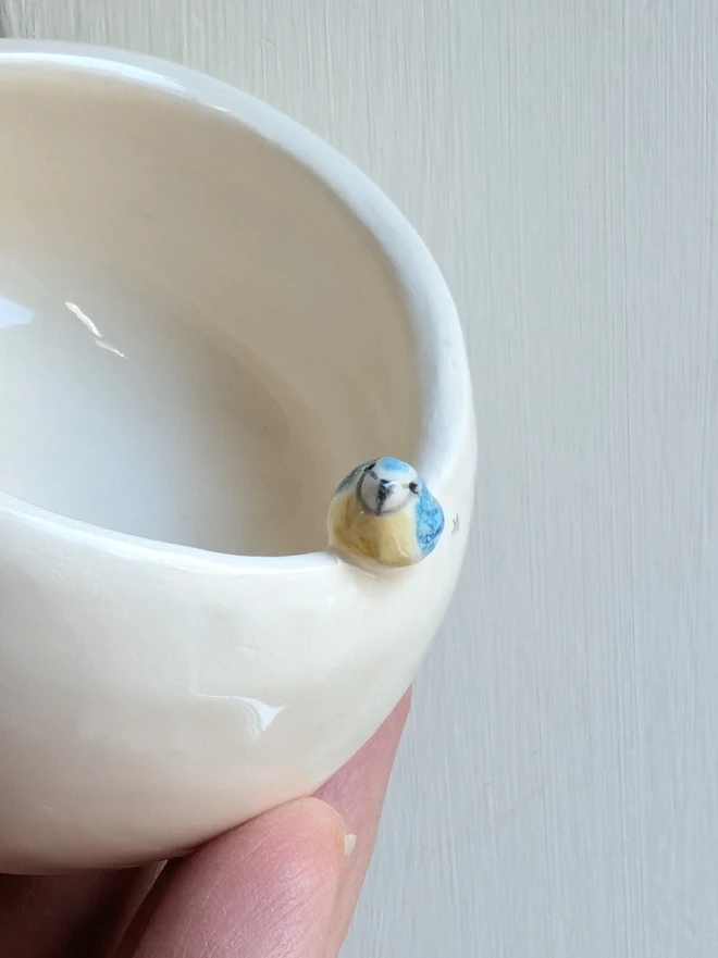 ceramic blue tit tea light with a miniature bird on the rim shown close up on a white pot