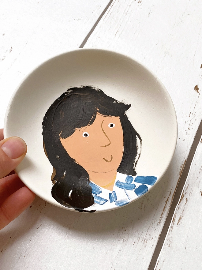 small white plate with stylised painted portrait of girl with striped blue and white shirt