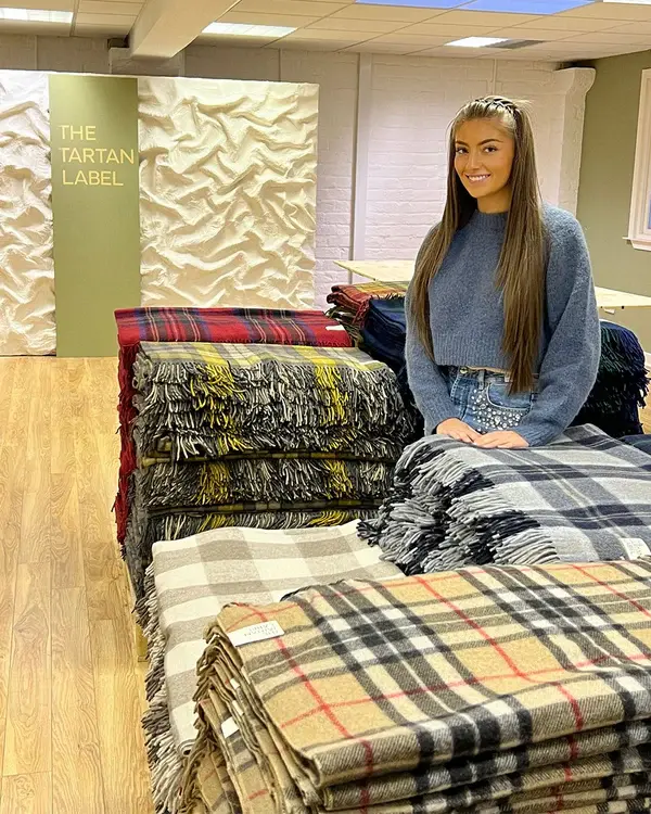 Daisy standing in a room of tartan blankets