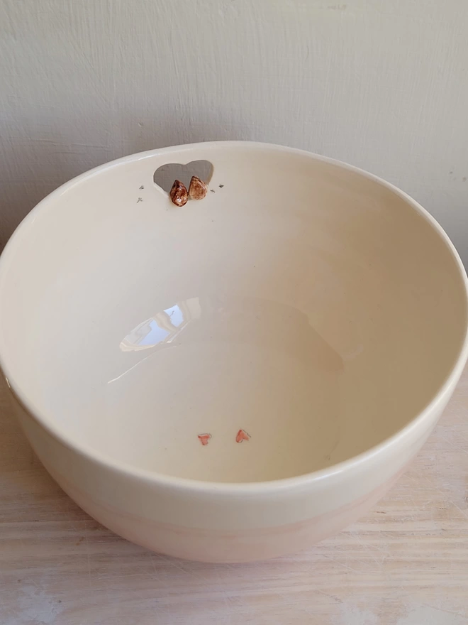the inside of a ceramic off white bowl showing the back view of two tiny robin birds perching in a cut out heart shape showing bird prints and 2 red hearts painted on the base