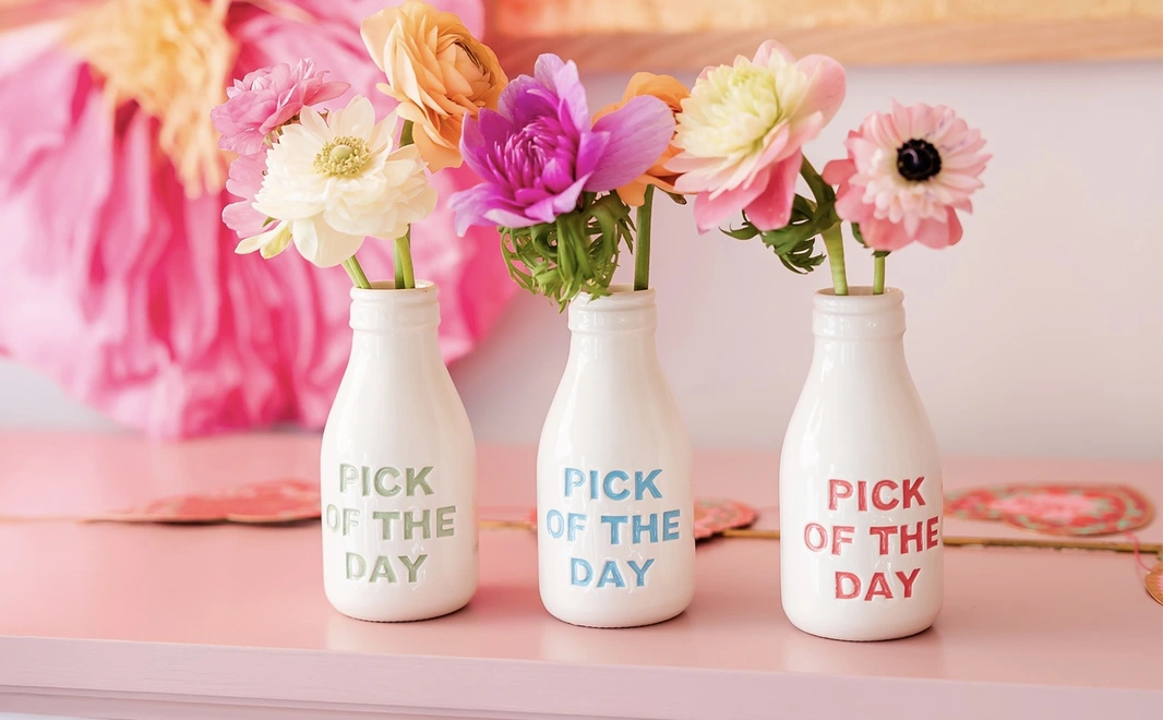 Pick of the day ceramic vase. Vase with different coloured lettering saying 'pick of the day' with small pink and yellow flowers inside.