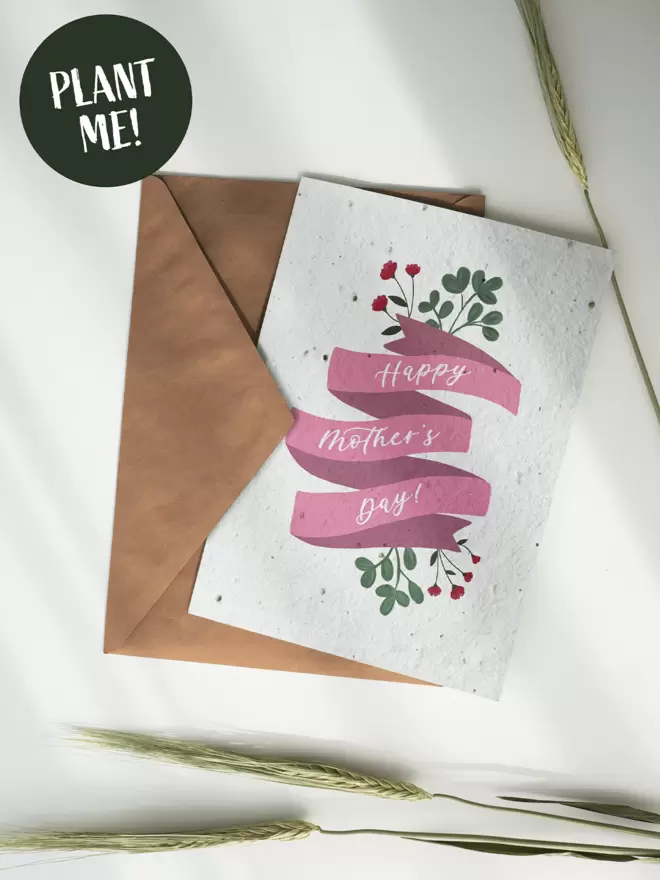 Card and brown envelope with 'Happy Mother's Day' on a pink banner with straws of wheat surrounding us.