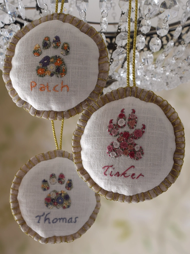 Finished embroidered Cat Paws and Dog Paw turned into felt baubles, displayed hanging from a crystal chandelier. 