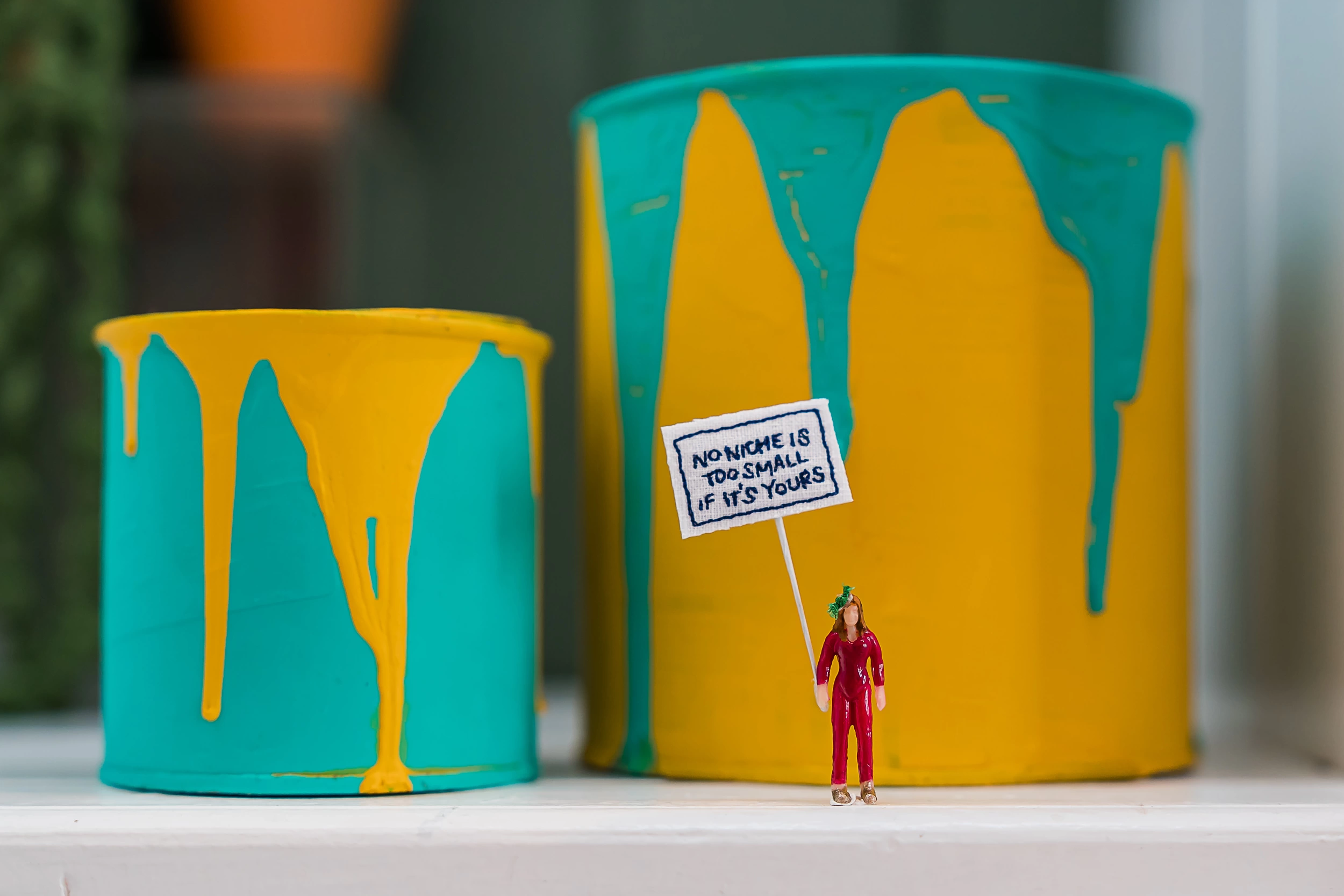 Two paint cans with small woman figurine holding sign no niche is too small if it's your niche 