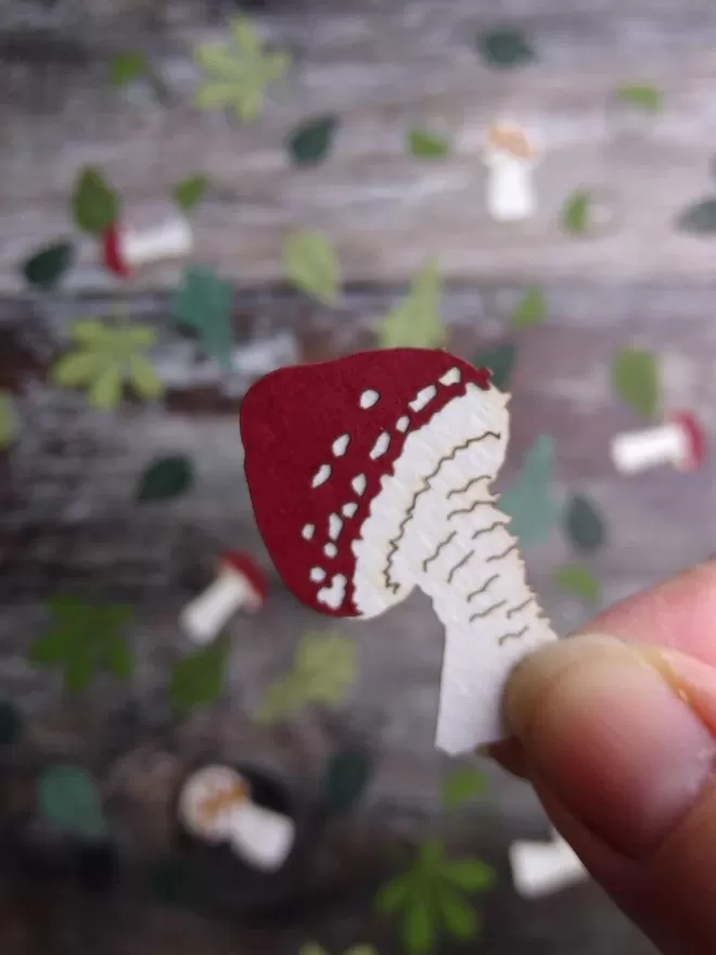 Woodland confetti toadstool piece.  Toadstool has white stalk and dark red cap with white spots.