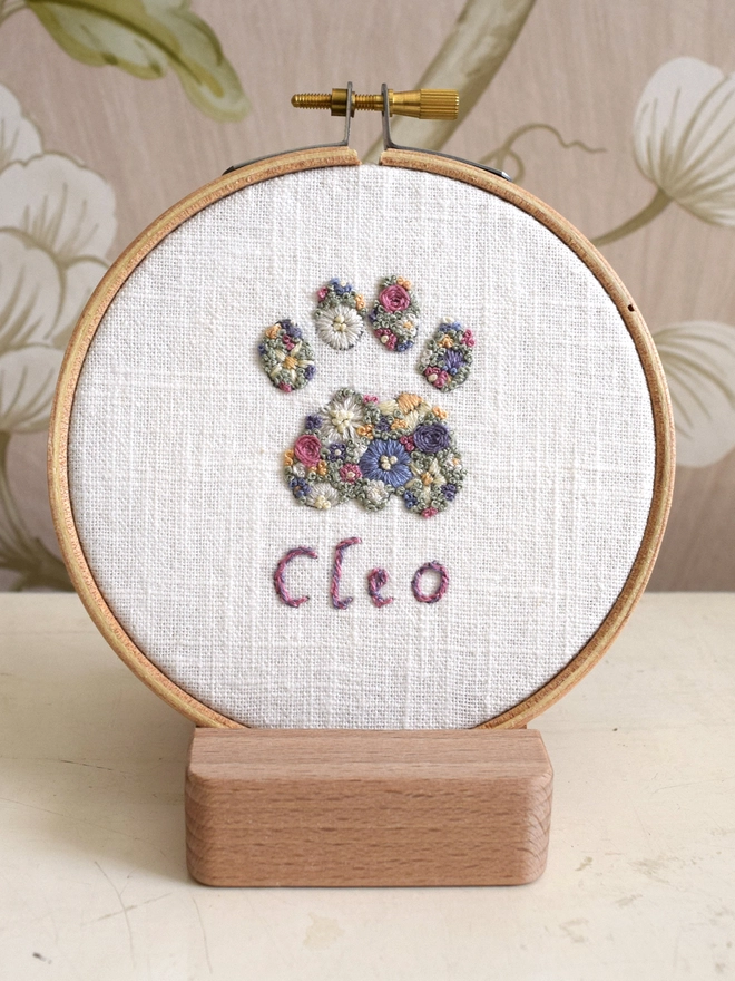 Floral Meadow Cat Paw, of Lavender Blues and Buttermilk yellow blossoms.  Displayed in an embroidery hoop on a wooden stand.