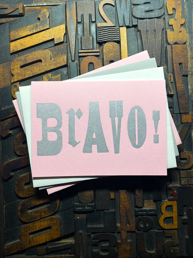 A congratulatory letterpress candy pink card featuring the deep impression word "BRAVO!"; in bold metallic gold letters with a set of colourful envelopes. Perfect for exam results and graduations and other celebrations and milestones.