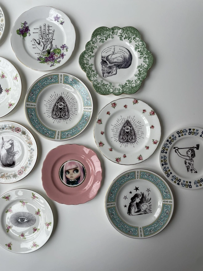 an eclectic collection of vintage plates hung together on a white wall, each plate is different with patterned or gold borders and vintage images in their centres