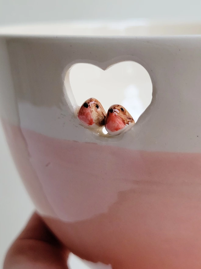 close up of a pink ceramic bowl with a heart cut out and two tiny robins perching in the heart 