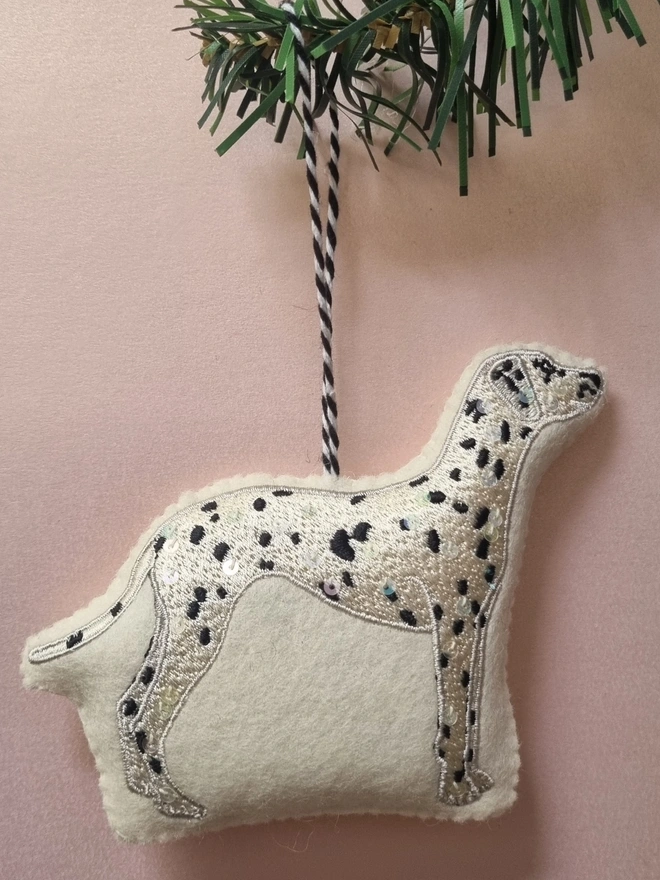 An embroidered dalmatian tree decoration on a pick background with a christmas tree branch