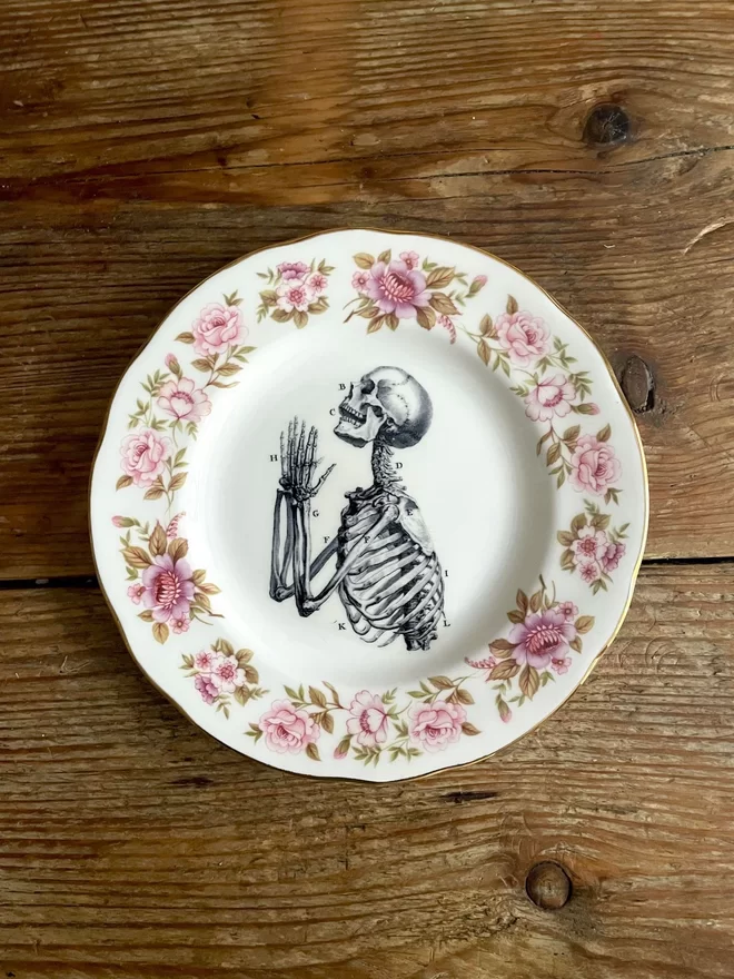 vintage plate with an ornate border, with a printed vintage illustration of a praying skeleton in the middle
