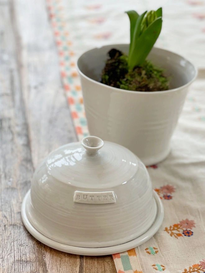 domed butter dish on pretty table runner with a hyacinth growing in a pot just behind the butter dish