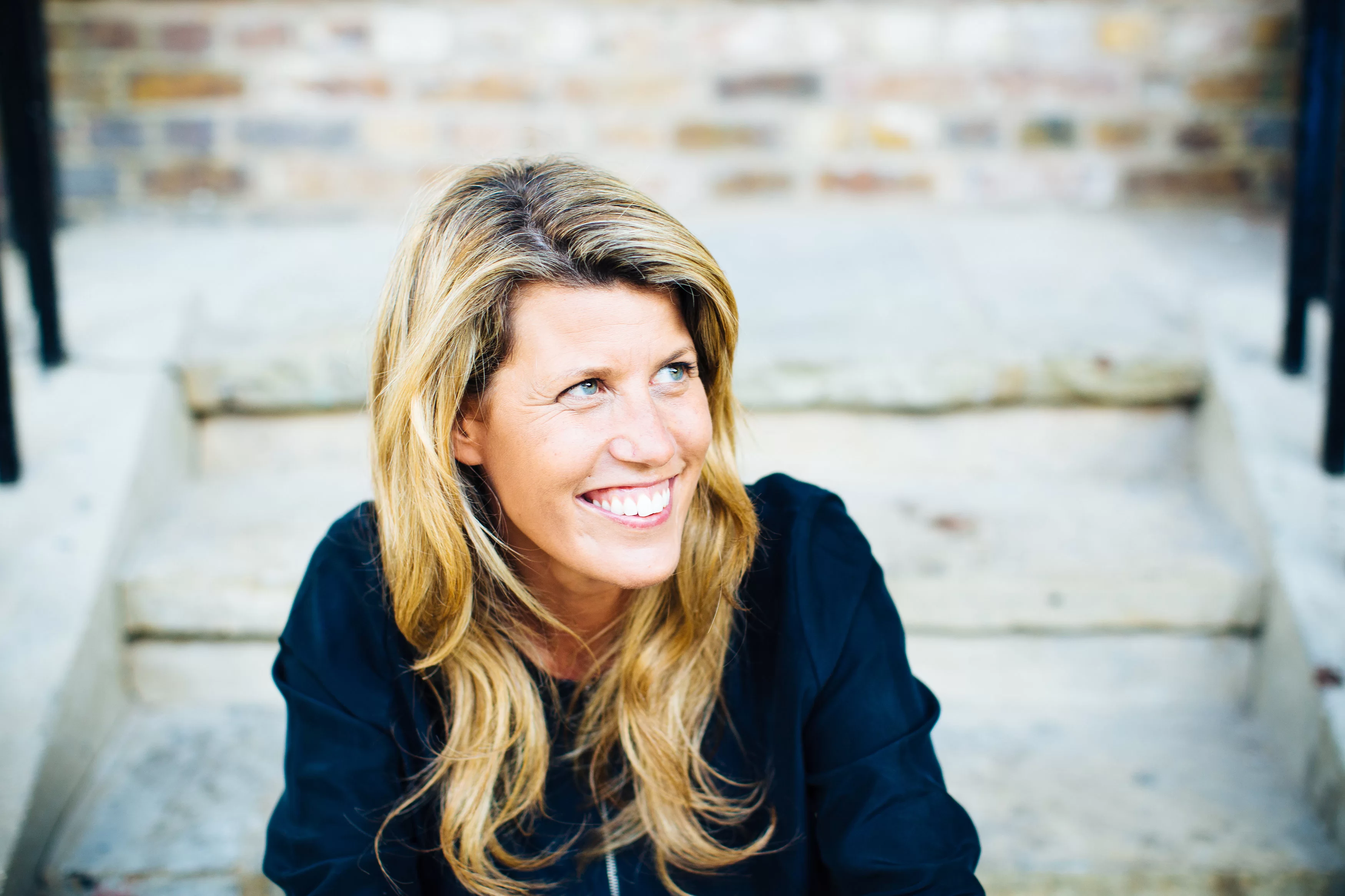 Pip Jamieson, founder of The Dots, sitting on some concrete steps and smiling. 