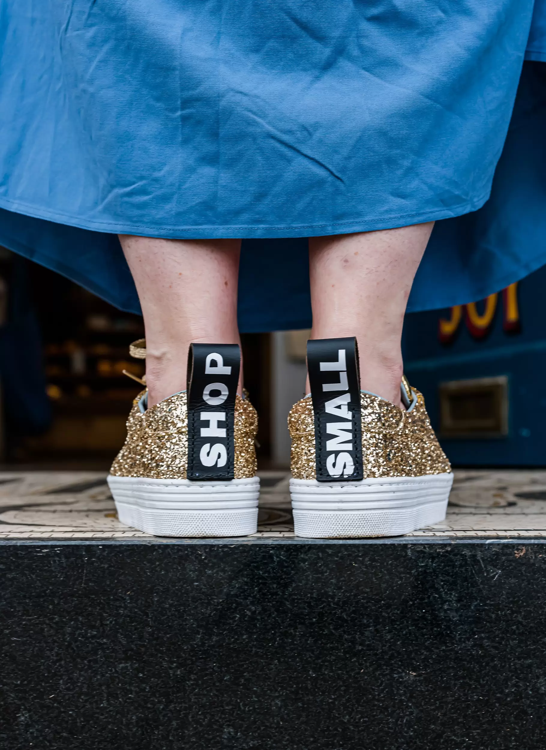 Holly Tucker, founder of Holly & Co, wearing a blue skirt and gold glitter trainers with shop small trim 