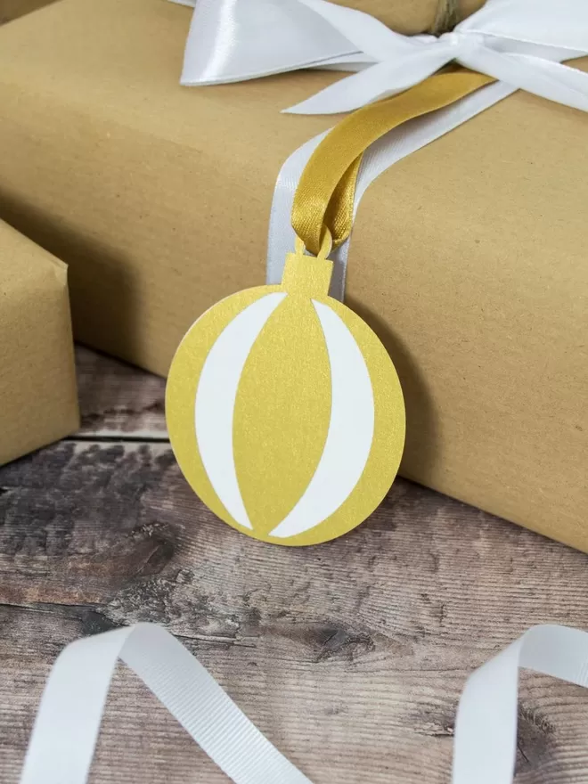 Gold bauble gift tag attached to gift wrapped in brown paper.