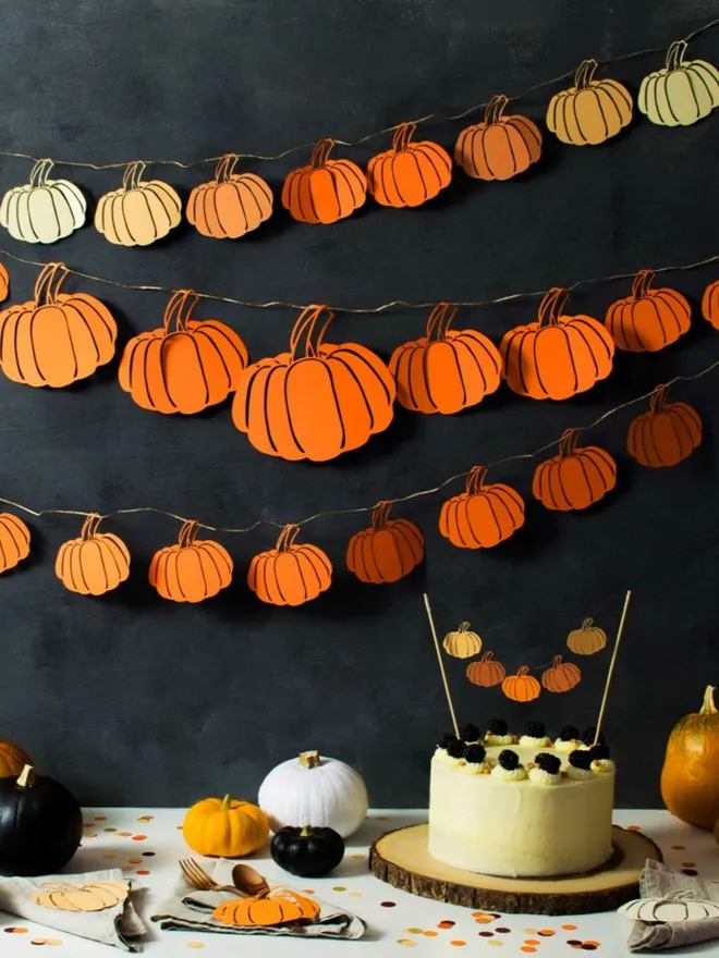 3 Pumpkin Garlands displayed on black wall. Garland one inlcudes paper pumpkins in a range of autumnal colours, garland two fatures orange pumpkins in a mix of sizes, garland three features orange pumpkin decorations