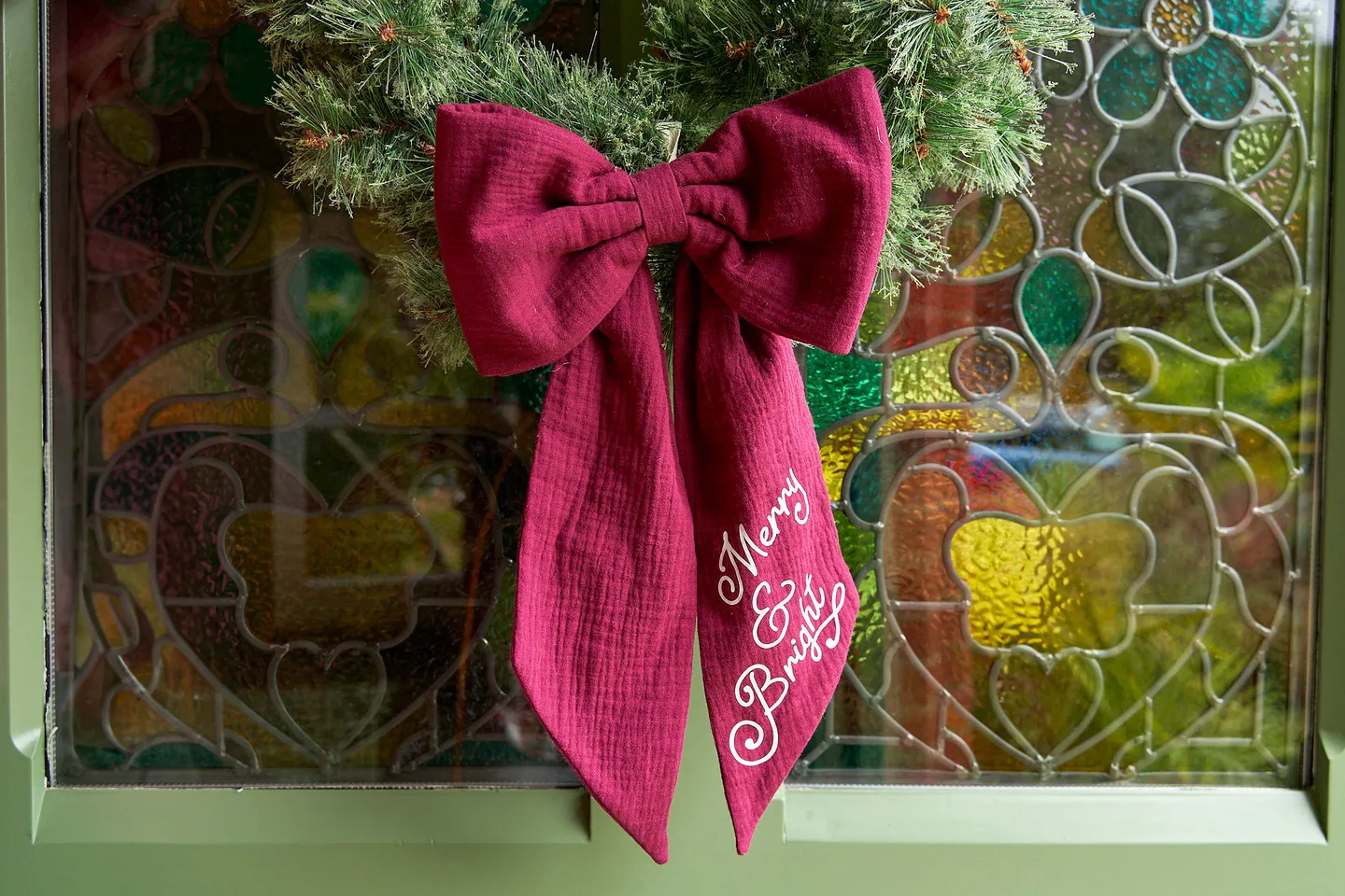 Merry and bright red Christmas bow. A burgundy red bow on a wreath with a stained glass window behind.