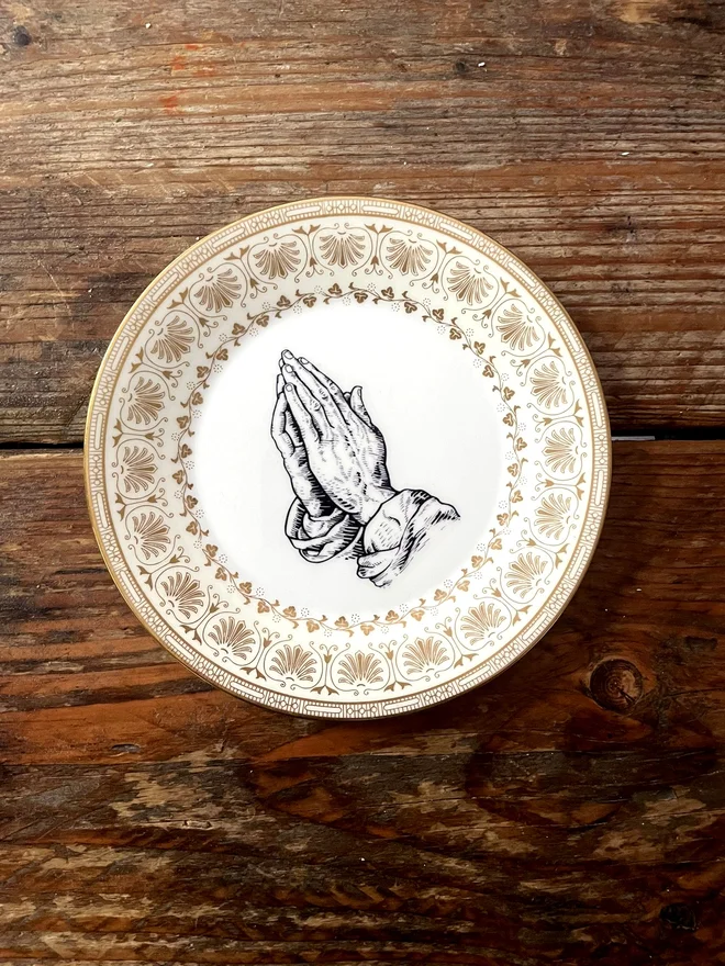 vintage plate with an ornate border, with a printed vintage illustration of a praying hands in the middle 
