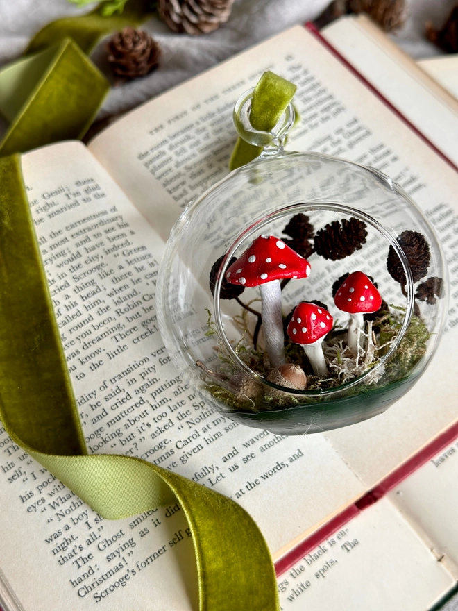 Glass Bauble filled with handmade toadstools and alder cones sitting on a vintage book 