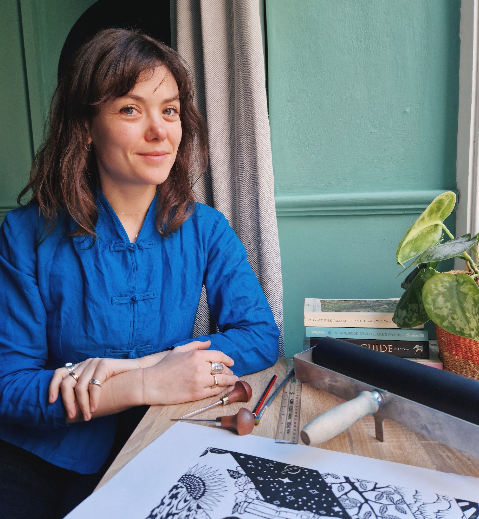 Rosanna Reade sits at a table with printmaking equipment