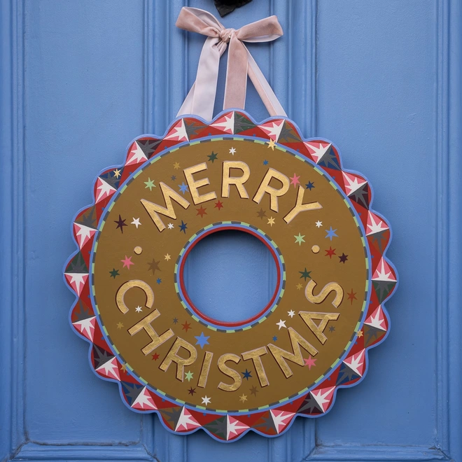 A colourful handpainted wooden wreath with the words merry christmas painted around the middle
