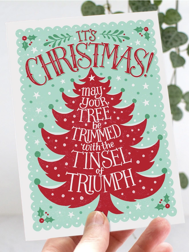 hand holding red and green tinsel christmas tree card