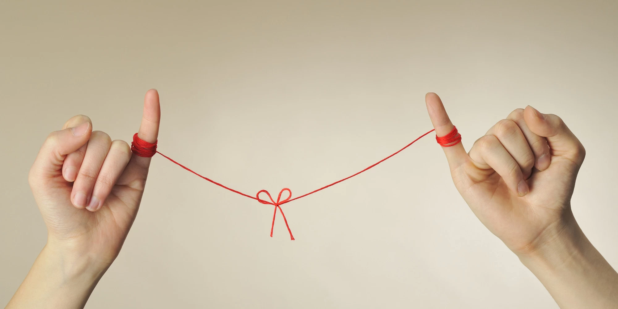 Two hands holding red string with a heart in the middle 