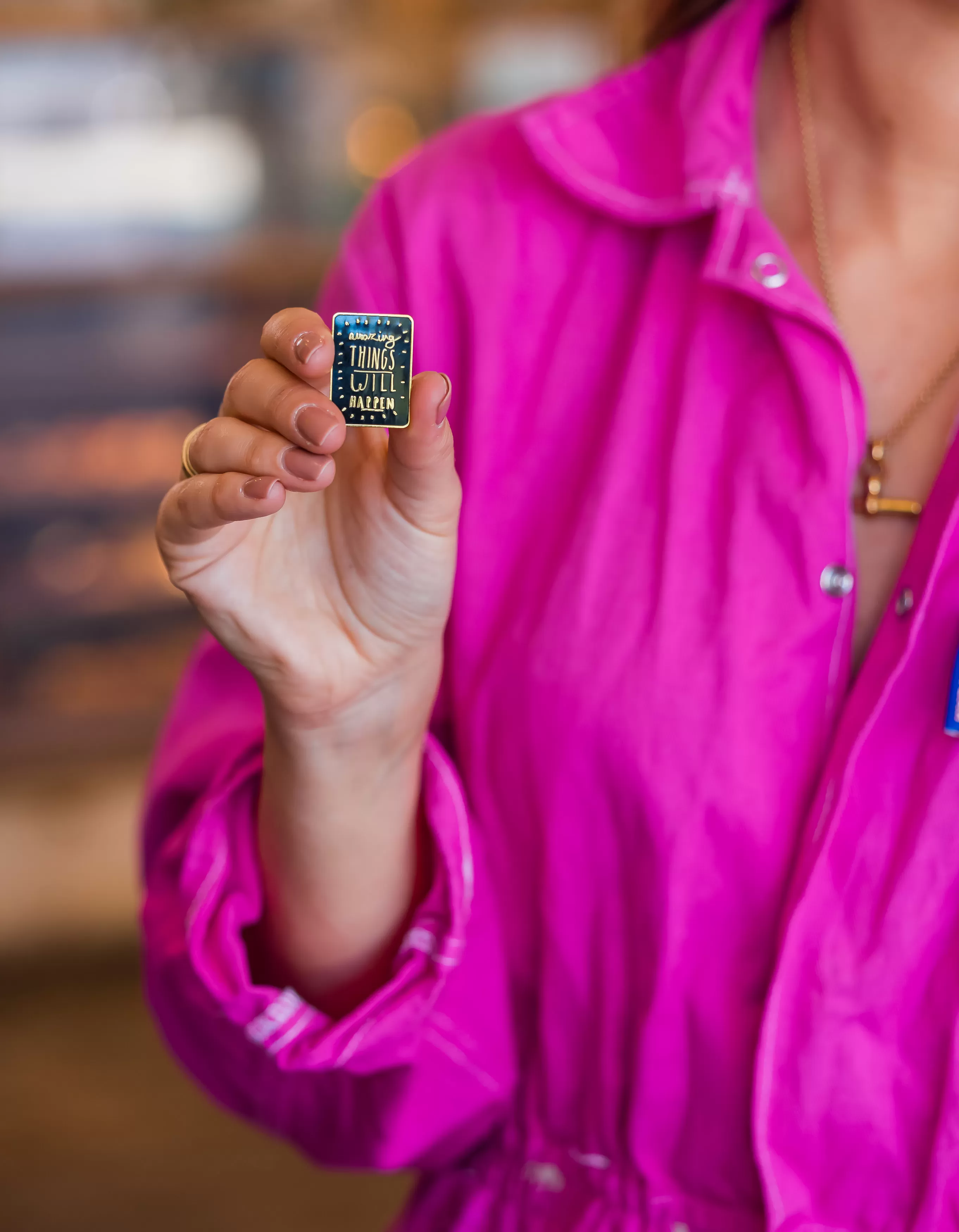 Woman wearing pink jumpsuit holding pin badge with words Amazing things will happen