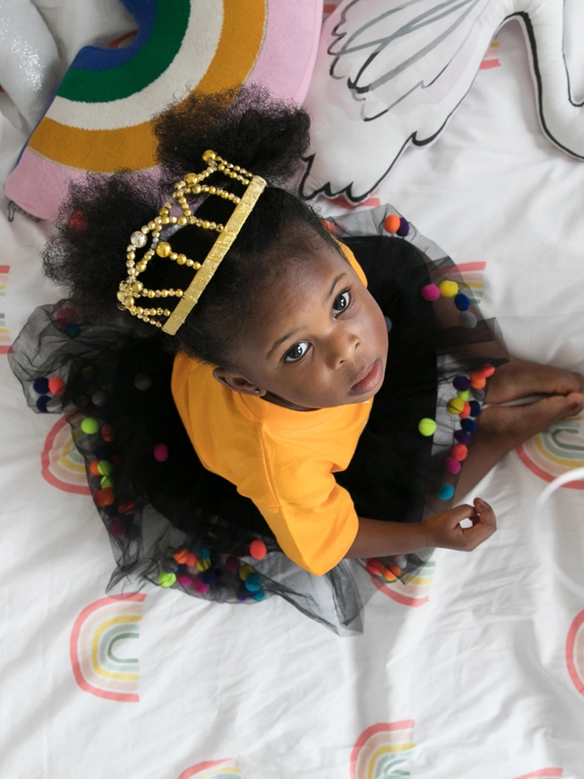 Little girl sitting, wearing a black pom pom tutu with neon pom poms