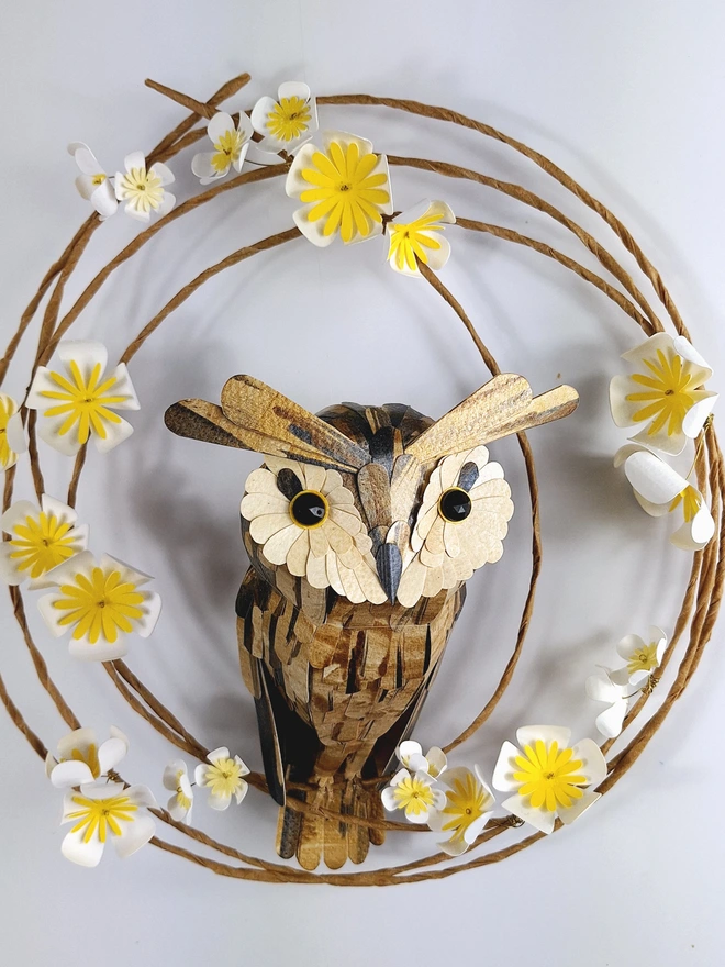 long eared owl sculpture perched on a wreath adorned with white and yellow tree blossom