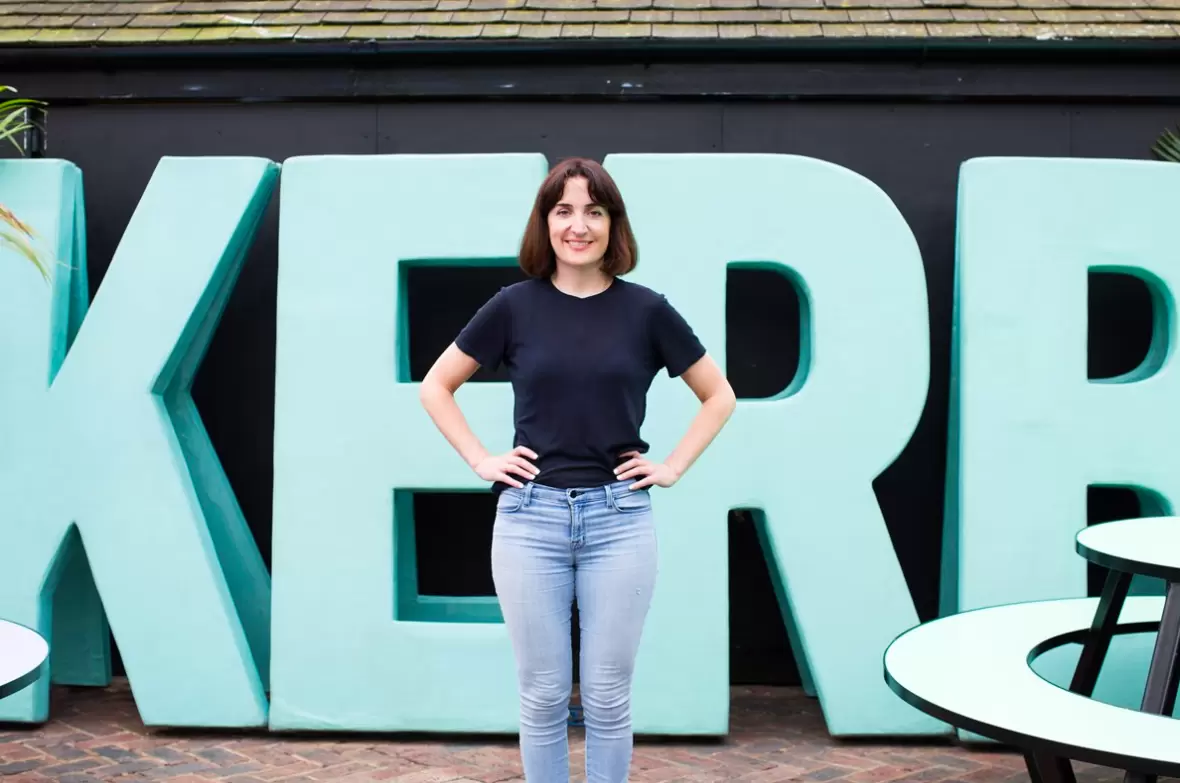 Petra Barran, founder of Kerb, smiling at the camera standing infront of a blue KERB sign.
