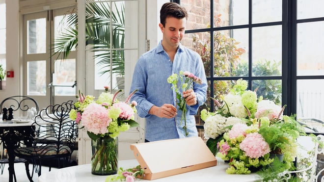 Aron Gelbard, co-founder of Bloom & Wild, wearing a blue shirt, looking at a bunch of flowers he is holding.