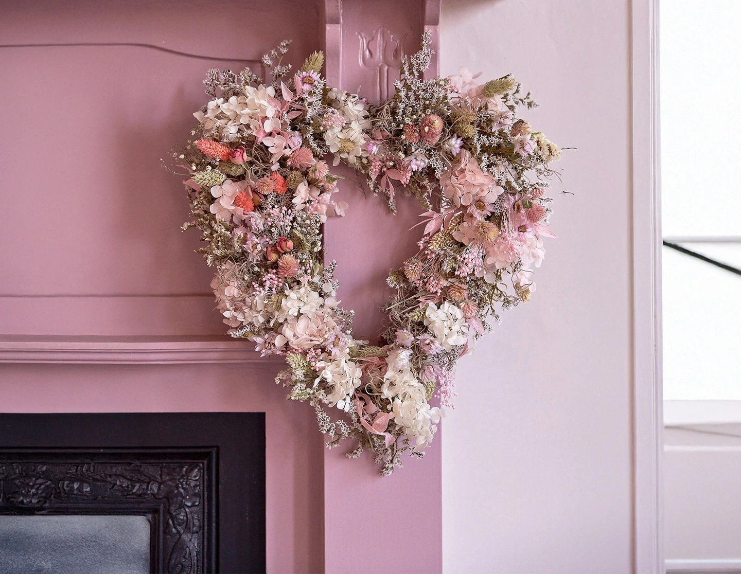 Heart spring wreath. A pink dried floral wreath in the shape of a heart on a pink mantlepiece