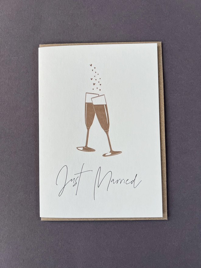 Two metallic bronze champagne flute glasses with bubbles coming from the top and "Just Married" beautifully written in a modern calligraphy underneath.