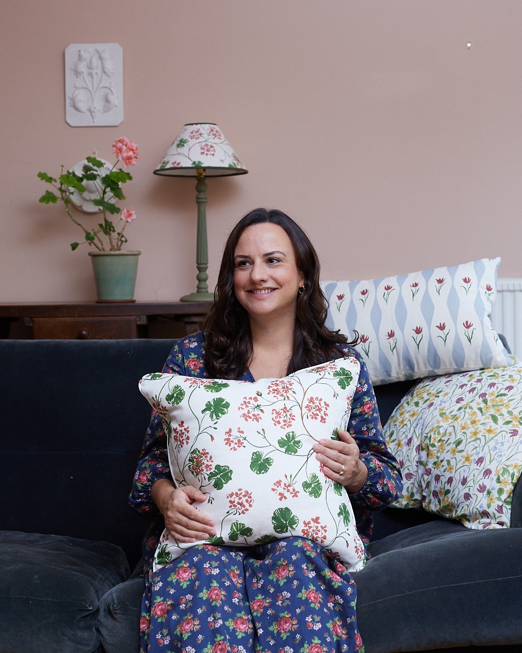 Artist and designer Sophie Harpley sitting on a sofa surrounded by her patterned cushions.