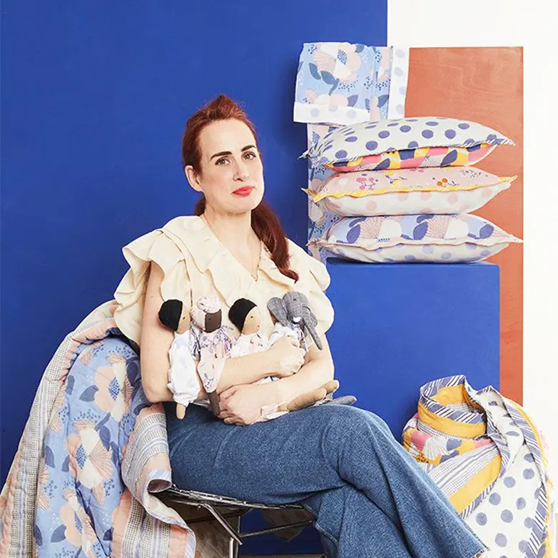 ai.no.ah founder Noa Alvarez sitting on a chair surrounded by block printed products including cushions and quilts