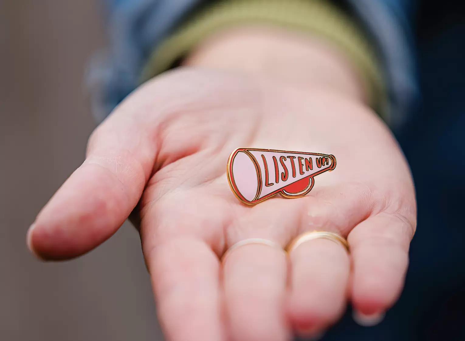 Hand holding out a pin badge saying listen up.