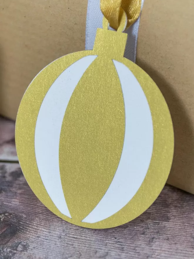 Closeup of round bauble gift tag.  Gift tag has a white base layer with frosted gold "beach ball segmented" top layerGold Christmas Ornament Gift Tags