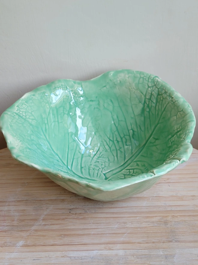 a green cabbage leaf ceramic bowl on a wooden surface