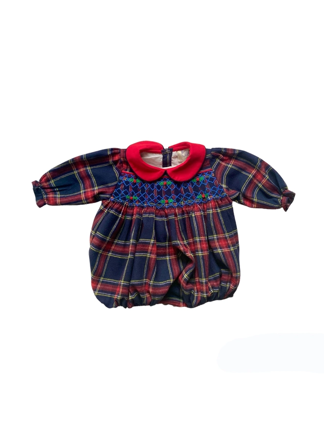 A navy and red tartan romper with a red contrast collar and hand smocking featuring holly embroidery