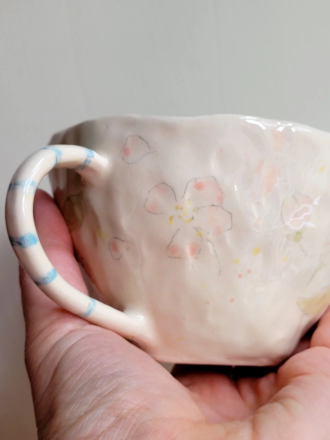 handmade pottery cup in white earthenware with hand painted pink blossom flowers and held in a hand w
