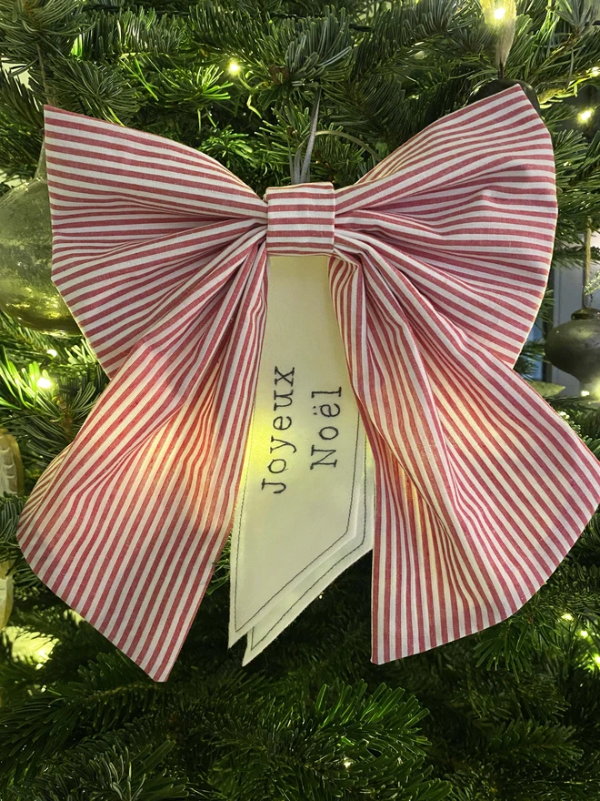 red stripe Christmas bow on Christmas tree with words joyeux noel