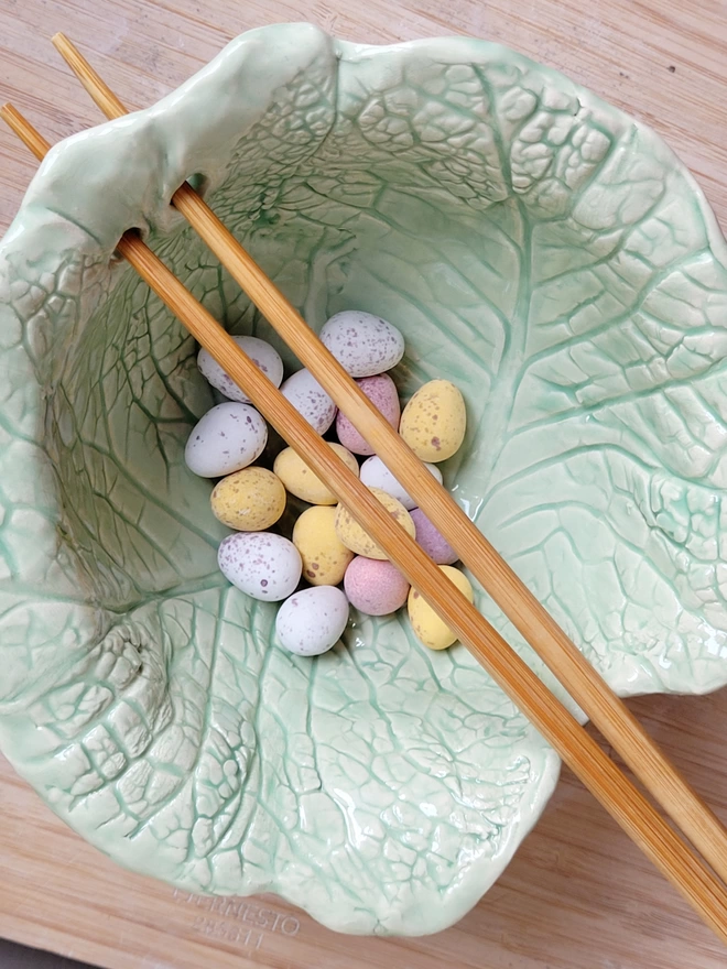 flat lay shot of a pale green noodle ramen bowl with lettuce or cabbage leaf design and chocolate mini eggs inside 