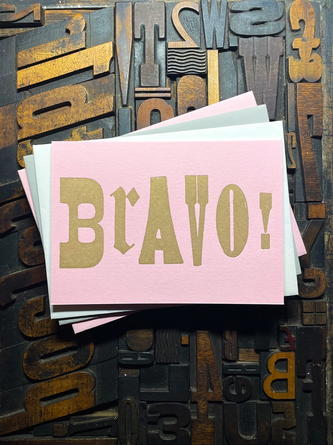 A congratulatory letterpress candy pink card featuring the deep impression word "BRAVO!"; in bold metallic gold letters with a set of colourful envelopes. Perfect for exam results and graduations and other celebrations and milestones.