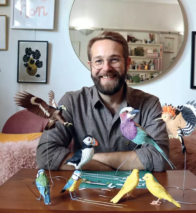 Zack McLaughlin, founder of Paper and Wood, smiling at the camera with bird sculptures in the foreground.