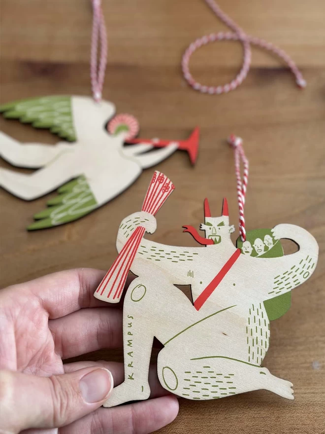 a hand holds a wooden christmas krampus, with an angel in background